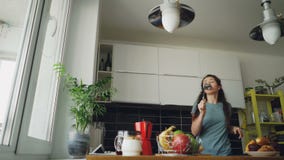Vrolijke jonge grappige vrouw die en met gietlepel thuis dansen zingen terwijl het hebben van vrije tijd in de keuken stock footage Vrolijke jonge grappige vrouw die en met gietlepel thuis dansen zingen terwijl het hebben van vrije tijd in de keuken stock footage