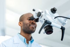 Vrolijke mannelijke tandarts die lens van microscoop onderzoeken stock afbeeldingen Vrolijke mannelijke tandarts die lens van microscoop onderzoeken stock afbeeldingen