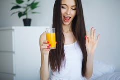 Vrolijke vrouw die een jus d'orangezitting op haar bed drinken bij ho Stock Afbeelding Vrolijke vrouw die een jus d'orangezitting op haar bed drinken bij ho Stock Afbeelding