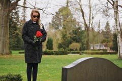 Vrouw die bij de bloemen van de begraafplaatsholding treuren stock foto's Vrouw die bij de bloemen van de begraafplaatsholding treuren stock foto's