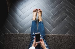 Vrouw die in in jeans op houten grijze vloer zitten, die lege het scherm mobiele telefoon houden achtergrond, Exemplaarruimte stock foto Vrouw die in in jeans op houten grijze vloer zitten, die lege het scherm mobiele telefoon houden achtergrond, Exemplaarruimte stock foto
