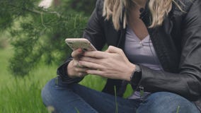 Vrouwenzitting op het gras met een telefoon in haar handen en een slim horloge voorraad Het concept technologieën binnen elke dag stock videobeelden Vrouwenzitting op het gras met een telefoon in haar handen en een slim horloge voorraad Het concept technologieën binnen elke dag stock videobeelden