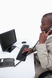 Vue de côté d'un secrétaire répondant au téléphone tout en employant un compu photos libres de droits Vue de côté d'un secrétaire répondant au téléphone tout en employant un compu photos libres de droits