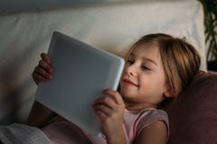 vue de côté de peu d'enfant à l'aide du comprimé dans le lit photo libre de droits vue de côté de peu d'enfant à l'aide du comprimé dans le lit photo libre de droits