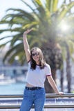 Vue de face d'une belle jeune femme de sourire utilisant les vêtements urbains et les lunettes de soleil se tenant tout en regard image stock Vue de face d'une belle jeune femme de sourire utilisant les vêtements urbains et les lunettes de soleil se tenant tout en regard image stock