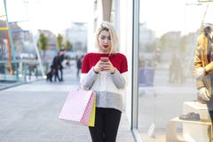 Vue de face d'une position de sourire de jeune femme à un centre commercial tout en à l'aide d'un téléphone portable photos libres de droits Vue de face d'une position de sourire de jeune femme à un centre commercial tout en à l'aide d'un téléphone portable photos libres de droits