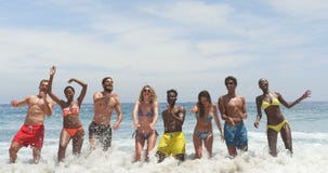 Vue de face des amis de métis sautant ensemble sur la plage 4k banque de vidéos Vue de face des amis de métis sautant ensemble sur la plage 4k banque de vidéos