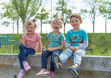 Vue de face des enfants passant le temps en parc, gar?on et filles de ville s'asseyant sur la pierre Fr?re et soeurs affectueux d photos stock Vue de face des enfants passant le temps en parc, gar?on et filles de ville s'asseyant sur la pierre Fr?re et soeurs affectueux d photos stock
