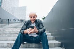 Vuxen skallig skäggig man som använder mobilen och sitter i trappa på stadsgatan arkivfoto Vuxen skallig skäggig man som använder mobilen och sitter i trappa på stadsgatan arkivfoto