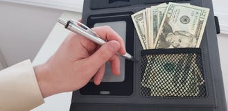Vänster hand med en penna över svart mapp med dollarsedlar i ett fack arkivbild Vänster hand med en penna över svart mapp med dollarsedlar i ett fack arkivbild