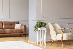 Växt på en stilfull vit trätabell i mitt av elegant vardagsrum med den retro fåtölj- och bruntlädersoffan royaltyfri fotografi Växt på en stilfull vit trätabell i mitt av elegant vardagsrum med den retro fåtölj- och bruntlädersoffan royaltyfri fotografi