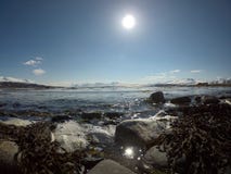 Vågor som slår den steniga kusten med den ljusa solen och det snöig berget Arkivbilder Vågor som slår den steniga kusten med den ljusa solen och det snöig berget Arkivbilder