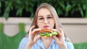 W górę portret szczęśliwej przyjemnej młodej kobiety je smakowitego grubego hamburger patrzeje kamerę zdjęcie wideo W górę portret szczęśliwej przyjemnej młodej kobiety je smakowitego grubego hamburger patrzeje kamerę zdjęcie wideo
