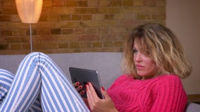 W górę strzał blondynki gospodyni domowej opowiada w videochat na pastylce w wygodnej domowej atmosferze w różowym puloweru lying zdjęcie wideo W górę strzał blondynki gospodyni domowej opowiada w videochat na pastylce w wygodnej domowej atmosferze w różowym puloweru lying zdjęcie wideo