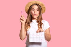 Waist up shot of amazed beautiful woman holds pen and menstrual calendar, shows five day marked with hearts, isolated over pink stock photo Waist up shot of amazed beautiful woman holds pen and menstrual calendar, shows five day marked with hearts, isolated over pink stock photo
