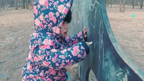 Weinig leuk meisje in een kleurrijk roze jasje trekt met krijt op een bord in de vorm van een dinosaurus op kinderen stock footage Weinig leuk meisje in een kleurrijk roze jasje trekt met krijt op een bord in de vorm van een dinosaurus op kinderen stock footage