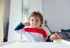 Weinig zitting van de peuterjongen als voorzitter voor het voeden in een ruimte in ontbijttijd royalty-vrije stock foto's Weinig zitting van de peuterjongen als voorzitter voor het voeden in een ruimte in ontbijttijd royalty-vrije stock foto's