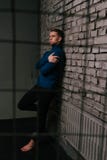 weißer attraktiver Mann in einer blauen Strickjacke und in schwarzen Hosen, barfüßigstände nahe einer Steinwand hinter Gittern ei stockbild weißer attraktiver Mann in einer blauen Strickjacke und in schwarzen Hosen, barfüßigstände nahe einer Steinwand hinter Gittern ei stockbild