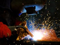 Welding steel and sparks. A tradesman welding steel on site at a engineering site at a mine. The sparks from the arc light the gloves and elding shield helmet Welding steel and sparks. A tradesman welding steel on site at a engineering site at a mine. The sparks from the arc light the gloves and elding shield helmet