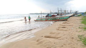 WELIGAMA, SRI LANKA - MÄRZ 2014: Die Ansicht von Booten auf dem Strand in Weligama mit den Leuten, die vorbei überschreiten Der A stock video WELIGAMA, SRI LANKA - MÄRZ 2014: Die Ansicht von Booten auf dem Strand in Weligama mit den Leuten, die vorbei überschreiten Der A stock video