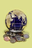 wereldeconomie - Mooie de bolzitting van de emailwereld op een stapel van muntstukken uit de hele wereld op gele achtergrond - se royalty-vrije stock afbeelding wereldeconomie - Mooie de bolzitting van de emailwereld op een stapel van muntstukken uit de hele wereld op gele achtergrond - se royalty-vrije stock afbeelding