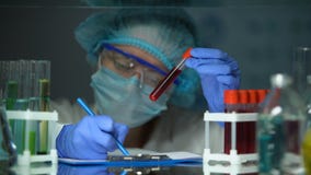 Wetenschapper die buis met bloedanalyse controleren en nota's, epidemische uitbarsting maken stock footage Wetenschapper die buis met bloedanalyse controleren en nota's, epidemische uitbarsting maken stock footage