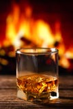 Whiskey in un vetro con fuoco nel camino sui precedenti immagini stock libere da diritti Whiskey in un vetro con fuoco nel camino sui precedenti immagini stock libere da diritti