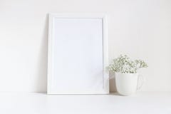 White blank wooden frame mockup with baby breath, Gypsophila flowers in porcelain mug on the table. Poster product