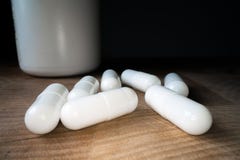 White pills or capsules next to bottle on wooden table background. Drug prescription, treatment medication. Pharmaceutical royalty free stock photo White pills or capsules next to bottle on wooden table background. Drug prescription, treatment medication. Pharmaceutical royalty free stock photo