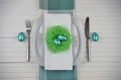 Springtime Easter table place setting in white with bright green handmade nest and blue shiny chocolate eggs stock photography Springtime Easter table place setting in white with bright green handmade nest and blue shiny chocolate eggs stock photography