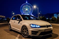 White vw golf in the evening next to the Ferris wheel.. View from the corner.