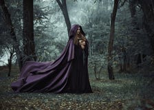 Wicked witch in a long dark cloak wandering in woods
