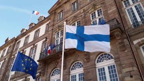 Wind blowing Finland and EU flags on the mast against blue sky background in front of Hôtel de Ville de Strasbourg, France.