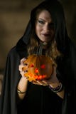 Beautiful witch in black mantle with a pumpkin face on Halloween stock photography Beautiful witch in black mantle with a pumpkin face on Halloween stock photography