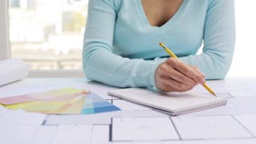 Woman with blueprint drawing interior to notebook