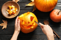 Woman carving Halloween pumpkin head jack lantern on wooden table