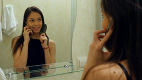 Woman combing her hair, preen and talking with her friend via smartphone in a hotel bathroom stock photography Woman combing her hair, preen and talking with her friend via smartphone in a hotel bathroom stock photography