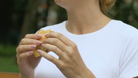 Woman eating burger, feels sudden pain in upper abdomen, gastritis, junk food