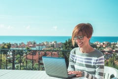 Woman with glasses and casual clothings working at laptop outdoors on terrace. Beautiful background of green hills and blue sky in royalty free stock images Woman with glasses and casual clothings working at laptop outdoors on terrace. Beautiful background of green hills and blue sky in royalty free stock images