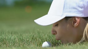 Woman golf beginner player lying on grass and blowing ball into hole, having fun stock footage Woman golf beginner player lying on grass and blowing ball into hole, having fun stock footage