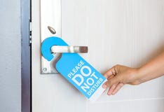 Woman hand holding signboard do not disturb hanging on the door. stock photo Woman hand holding signboard do not disturb hanging on the door. stock photo