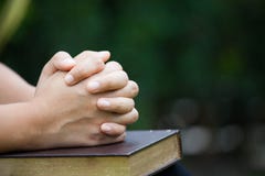 Woman hands folded in prayer on a Holy Bible for faith concept