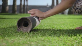 Woman hands rolling up yoga mat after training in park.Girl folding mat on grass