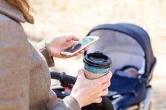 Woman holding cup of coffee to go and using smartphone during walk with baby carriage. Modern young business woman stock images Woman holding cup of coffee to go and using smartphone during walk with baby carriage. Modern young business woman stock images
