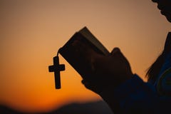 Woman holding a holy bible and cross in her hands and praying in the morning. Hands folded in prayer on a Holy Bible in church