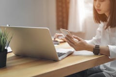 Woman holding smartphone and using laptop on table in office room on windows with trees and nature background. stock image Woman holding smartphone and using laptop on table in office room on windows with trees and nature background. stock image