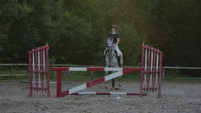 A woman jockey in a black and white suit on a horse makes a jump over the barrier. Slow motion: a woman jockey in a stock video footage A woman jockey in a black and white suit on a horse makes a jump over the barrier. Slow motion: a woman jockey in a stock video footage