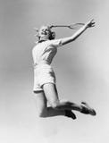 Woman jumping into the air with a tennis racket in her hand