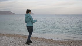 Woman at lonely cold beach. Caucasian woman throws stones into the calm sea. stock video footage Woman at lonely cold beach. Caucasian woman throws stones into the calm sea. stock video footage