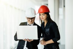 Woman and man entrepreneur and architect in hemlet at business meeting, looking at the laptop on building plans stock photo Woman and man entrepreneur and architect in hemlet at business meeting, looking at the laptop on building plans stock photo